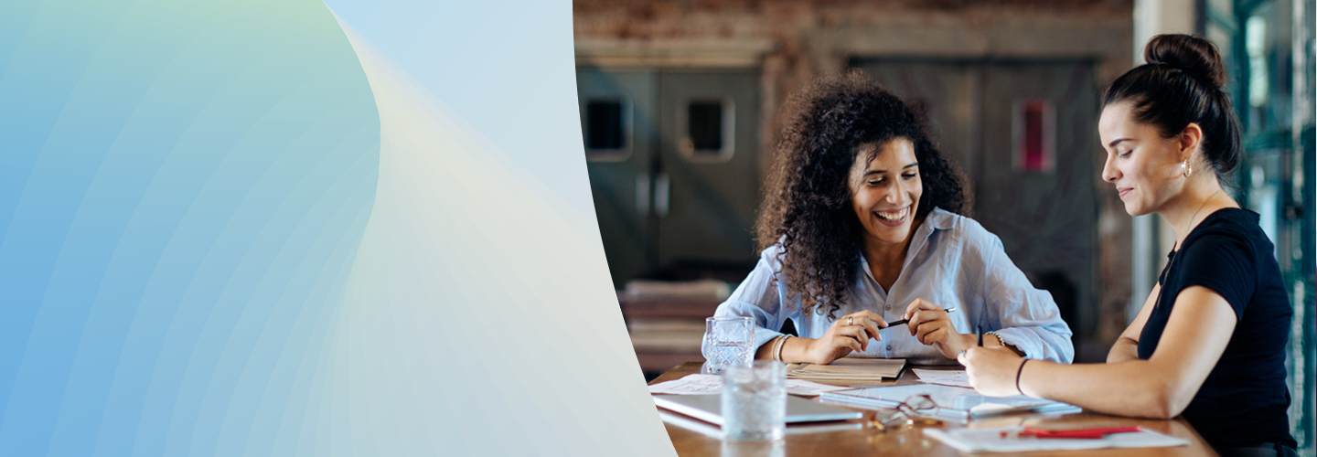 Two people sitting at a table with notebooks and a tablet.