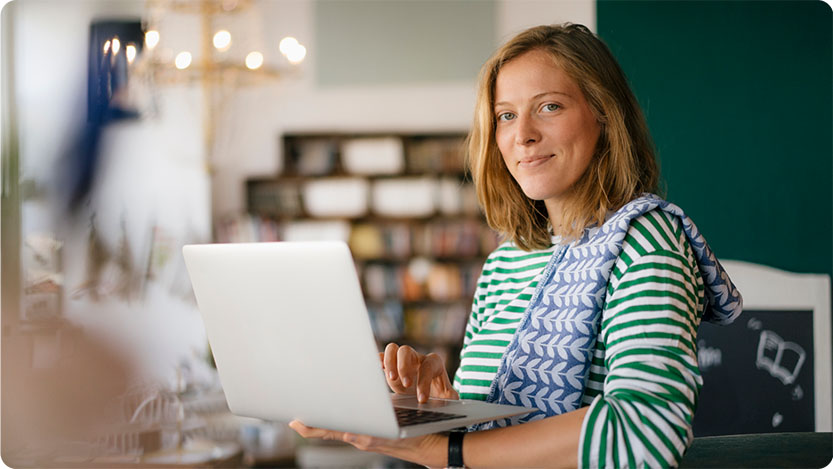 A person wearing a green and white striped shirt and a patterned scarf is using a laptop.      