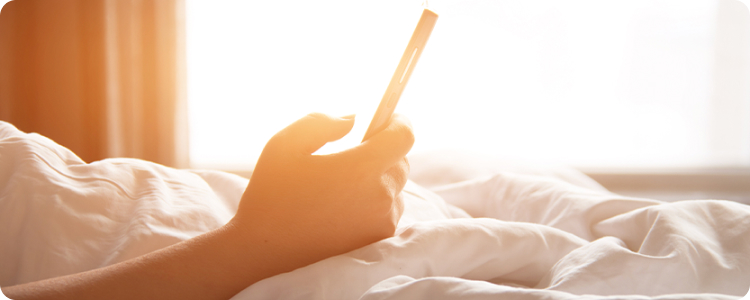Hand holding a smartphone above blankets in morning light